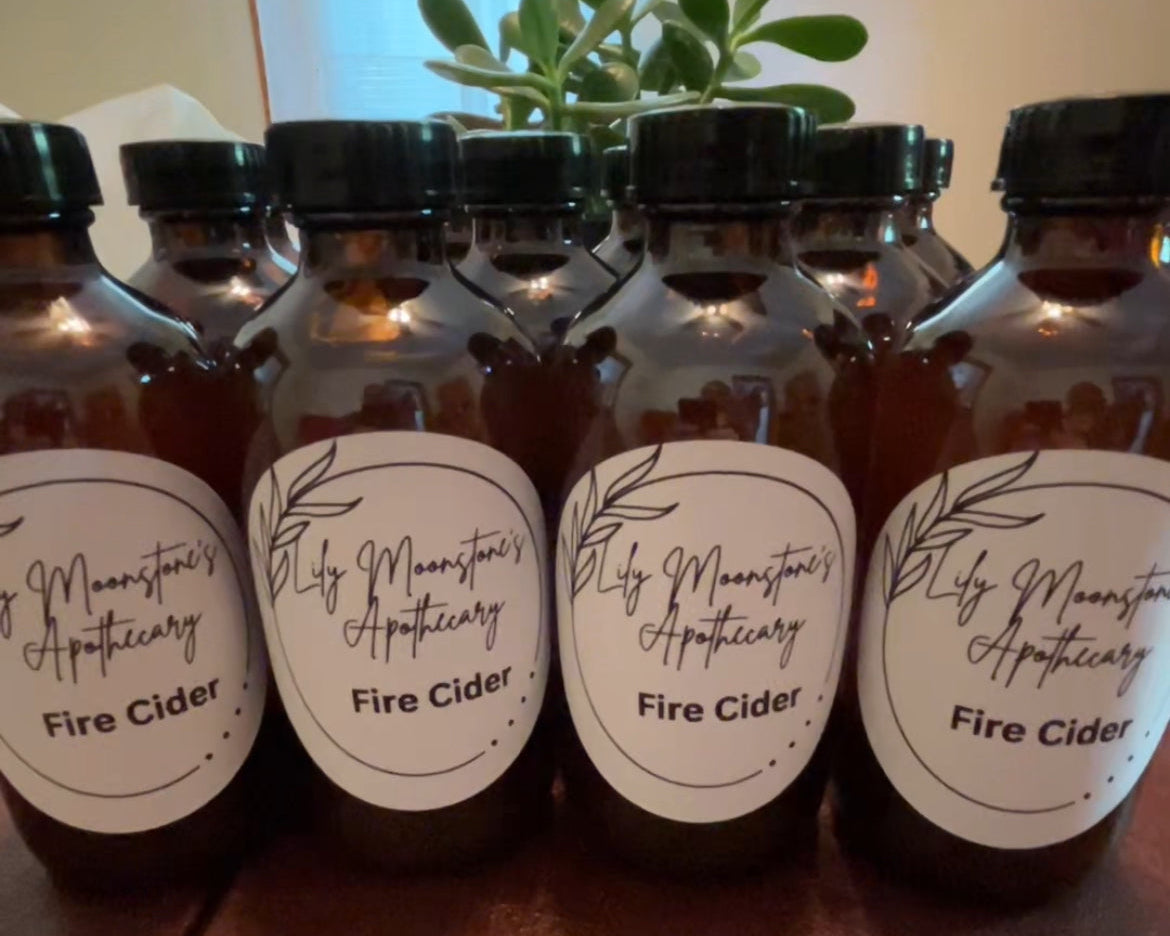 Bottles of Lily Moonstone Apothecary Fire Cider on a wooden surface with a plant in the background.